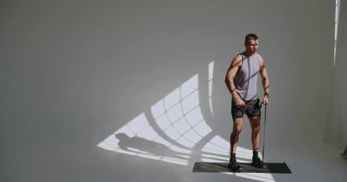 23 yaşında atletik yapılı bir adam parlak bir stüdyoda dayanıklılık ve zindelik üzerine çalışan bir direniş bandı kullanıyor. Genç Atletik Adam Stüdyoda Direniş Grubu Eğitimine Başladı