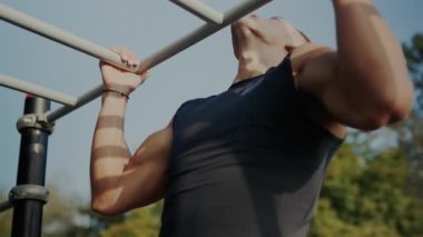 Güneşli bir günde parkta barfiks çeken genç adam. Sakin bir parkta barfiks çekme parmaklıklarına odaklanmış genç erkek eğitimi, dayanıklılık ve zindelik gösteriyor..