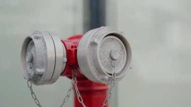 Zincirlerle korunan parlak kırmızı bir yangın musluğunun toz kaplı kapaklarını yumuşak odaklı arka planda gösteren detaylı bir yakın çekim görüntüsü. Toz kaplı kapaklı bir yangın musluğunun yakın çekim görüntüsü