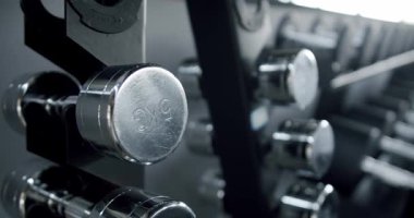 Spor salonunda asılmış çelik dambılların yakın plan görüntüsü, metalik dokusunu ve spor salonunu vurguluyor. Modern Spor Salonundaki Dambıllara Odaklanmış Görünüm