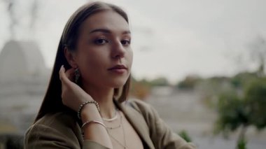 Gelişigüzel giyinmiş esmer bir kadının yakın plan portresi, şehir manzarası bulanık bir şehir ortamında düşünceli bir şekilde poz veriyor. Genç Kadın Düşünerek Şehir Arkaplanına Karşı Poz Veriyor