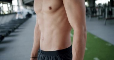 Formda genç bir adamın vücudu, spor salonunda kaslarını gösteriyor, fitness, sağlık ve adanmışlık temalarını çağrıştırıyor. Spor salonundaki fit genç adam kaslı gövde ve karın kaslarıyla hava atıyor.