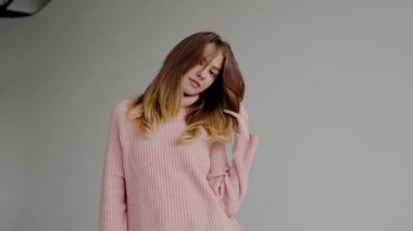 Gri arka planda pembe bir kazak ve kot pantolon giyen neşeli genç bir kadın. Moda ve yaşam tarzı temaları için mükemmel bir imaj. Pembe Süveterli Genç Kadın Stüdyoda Poz Veriyor