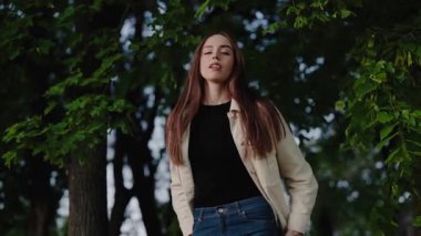 Genç kadın yemyeşil bir ormanda sakince duruyor güneşli bir günde doğanın huzur ve güzelliğinin tadını çıkarıyor. Güneşli bir günde Bahar Ormanı 'nda Doğanın tadını çıkaran Genç Kadın