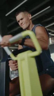 Modern bir spor salonunda kürek çeken odaklanmış bir adam. Spora adanmış bir ortamda spor eğitimi, egzersiz ve dayanıklılık. Spor salonunda Kararlı Adam Antrenmanı. Dikey