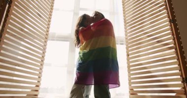 Çift, Lgbt ve lezbiyen kadınlar evde. Sarılın, gülümseyin ve bayrak sallayın. Aşk ve öpücük, iki kadın el ele tutuşarak sevgi ve desteği paylaşıyor. Yaşam tarzı ve ilişkiler. LGBT kavramı