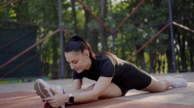 Atletik giyinen genç bir kadın güneşli bir parkta egzersiz yapıyor ve yoğun bir şekilde antrenmanına odaklanıyor. Park 'ta Gerinen Genç Kadın, Spor Salonu