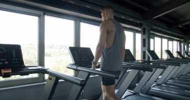 Geniş, iyi donanımlı bir spor salonundaki koşu bandına odaklanmış bir adam büyük pencerelerden manzaraya bakıyor. Şehir Manzaralı Modern Spor Salonunda Koşu Yapan Adam