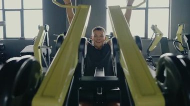 Genç adam spor salonundaki ağırlık makinesini kullanmaya odaklanmış. Fitness meraklısı kas geliştirme ve fiziksel zindeliği geliştirme eğitimi alıyor. Genç adam vücut çalışıyor.