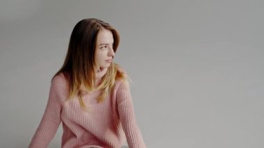 Rahat pembe bir kazak ve kot pantolon giymiş rahat rahat oturan genç bir kadının huzurlu portresi. İnce ifadesi rahatlatıcı, içsel bir ruh hali sergiliyor. Gençlik ve tarz temaları için mükemmel..