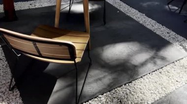Modern bir kafede boş sandalyeler ve masa. Güneş ışığı ve gölgeler sakin ve davetkar bir atmosfer yaratır. Restoranlar, kafeler, rahatlama ve kentsel yaşamla ilgili projeler için mükemmel.