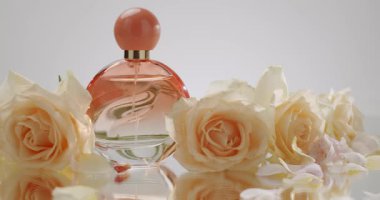 Zarif beyaz güllerle çevrili sofistike bir parfüm şişesine yakından bakın. Yansıtıcı bir yüzeyde, güzelliği, zarafeti ve lüksü tasvir ediyor. Zarif Parfüm Şişesi Çevrildi