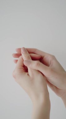 Zarif manikürlü, birbirine nazikçe masaj yapan, temiz, beyaz bir arkaplan üzerine kurulmuş ellerin yakın çekimi. Görüntü, rahatlama, özgüven ve güzellik taşır..