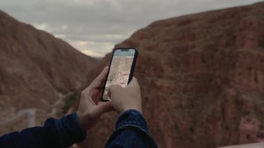 Birisi telefonuyla Fas manzaralı bir manzaranın fotoğrafını çekiyor. Uçsuz bucaksız tepeler ve vadiler doğanın güzelliğini yansıtan nefes kesici bir manzara yaratıyor..