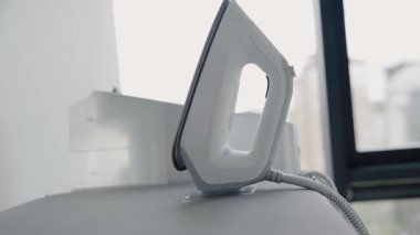 Modern elektrikli ütüyü parlak, minimalist bir iç mekandaki ütü masasına yakın çekim. Ev işleri, temizlik ve ev aletleri kavramları için mükemmel..