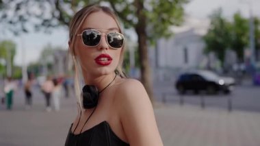 Canlı şehir ortamında parlak kırmızı dudakları ve güneş gözlükleriyle şık bir kadının yakın çekimi. Moda kadını kendine güvenen bir ifadeyle şık bir görünümü kucaklıyor. Şık Genç Kadın Yürüyüşü