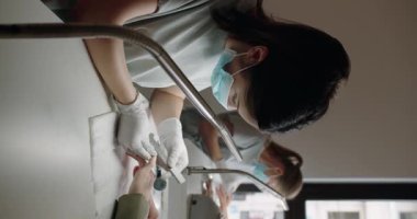 Güzellik salonunda manikür yaptıran kadın müşteri. Spa tedavisi. Koruyucu maskeli manikür ustası ve eldivenli müşteri tırnaklarını törpülüyor ve güzellik salonunda el bakımı yapıyor. Dikey video.