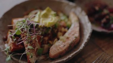 Avokado dilimleri ve taze yeşilliklerle servis edilen lezzetli ızgara somon salatasının yakın çekimi. Fırında balık, taze avokado, roka ve sebzelerle dolu bir kâse.