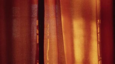 Altın güneş ışığı kırmızı bir perdeden geçerek sıcak ve davetkar bir atmosfer yaratır. Hafif bir esinti kumaşı hareket ettirir ve olay yerine sükunet katar. ev, konfor ve rahatlama.