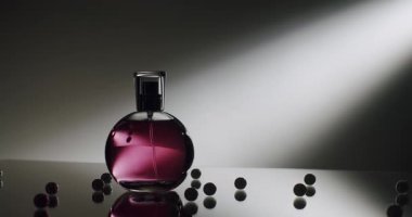 Dekoratif boncuklarla yansıtıcı bir yüzeyde şık, mor bir parfüm şişesinin yakın çekimi. Kaliteli parfüm, güzellik ve moda kavramları için mükemmel..