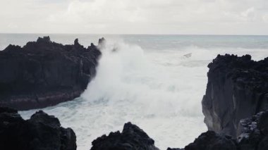 Güçlü okyanus dalgalarının engebeli kayalıklara çarpmasının çarpıcı görüntüsü. Sahne vahşi, dramatik ve doğanın saf gücünü ve güzelliğini sergiliyor..