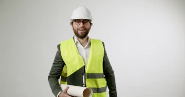 Kendine güvenen bir mimar ya da mühendis yaklaşırken elinde planlar ve bir pano ile gülümsüyor. Bina planlarını tartışmaya hazır profesyonellik ve uzmanlık yayıyor..
