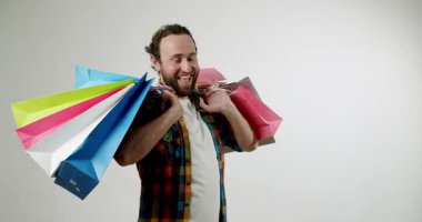 Mutlu adam beyaz arka planda bir sürü renkli alışveriş torbası taşıyor. Gülümsüyor ve alımlarından memnun görünüyor. Perakende terapi, indirim ve satış reklamları için harika..