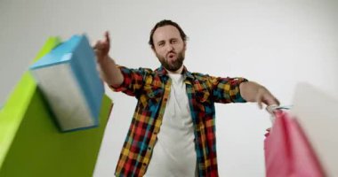 Alışveriş torbalı mutlu adam. Adam alışveriş yaptıktan sonra neşe ve memnuniyet gösteriyor. Beyaz arka planda erkek ellerinde renkli alışveriş torbaları. Yavaş çekimde video.