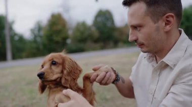 Bir erkek sakin bir park ortamında sevimli Cocker Spaniel köpeğiyle güzel vakit geçirmekten hoşlanır. Köpek yavrusu patisini kaldırır ve sahibinin nazikçe onu tutması gibi neşeli bir jest yapar. Altın Cocker Spaniel Köpek.