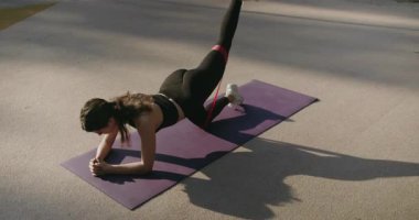 Spor giyinen esmer kadın sporcu, direniş bandıyla tahtada kal ve bacağını kaldır. Yoga tahtası pozu veren bir kadın. Direniş bandıyla egzersiz yapan genç bir kadın.. .