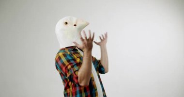 Kuş maskesi takan bir adam elleri beyaz bir arka planda hareket eder. Kendinden emin değil, kafası karışık ve belki biraz da deli..