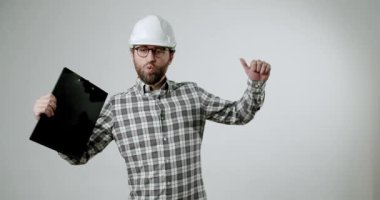 Neşeli bir erkek mimar ya da mühendis gözlük takıyor ve elinde bir pano tutarken şapka takıyor. Basit bir arkaplan karşısında mesleğinin başarısını ve neşesini dile getiriyor..