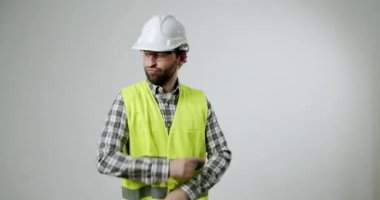 Kasketli ve güvenlik yeleği giyen bir inşaat işçisi beyaz arka plan önünde dans ediyor. Mesleğine olan tutkusunu gösteriyor ve her anından zevk alıyor. İnşaat için harika.