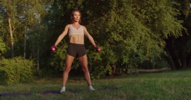 Atletik kadın dışarıda halterlerle egzersiz yapıyor. Kas Kol Sporu Egzersizi. Güçlü Fitness Vücut Egzersizi. Yağ yakma egzersizi. Spor giyim fitness. Fitness Egzersizi Spor Eğlencesi.