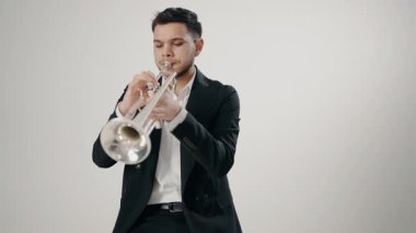 Takım elbiseli genç bir adam arzu ve ilhamla trompet çalar. Modern bir stüdyoda beyaz arka planda trompet çalan bir erkek caz şarkıcısı. Genç trompetçinin eli.