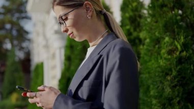 Gösterişli bir iş elbisesi içindeki genç profesyonel bir kadın şehir ortamında dışarıda dikilirken akıllı telefonunu dikkatle kullanır. Şehir Ayarlarında Akıllı Telefon Kullanan Profesyonel Kadın
