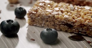 Taze yaban mersinleri ve hafif ahşap bir yüzeyde sergilenen besleyici bir granola barı içeren yakın plan bir görüntü. Sağlıklı bir atıştırmalık ve dengeli bir diyetin mükemmel tasviri. Yabanmersinli granola çikolataları