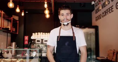 Modern kahve evinde kollarını kavuşturmuş dururken gülümseyen ve kameraya bakan genç bir erkek. Kahve dükkanında çalışırken gülümseyen genç adam.. 