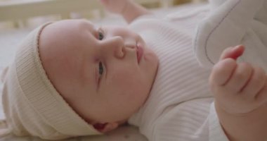 Bebek bezi takmış, yatakta uzanmış kameraya bakan tatlı bir bebek. Yatak çarşaflarına uzanmış, ayak parmaklarıyla oynuyor. Gülümsüyor, kameraya bakıyor..