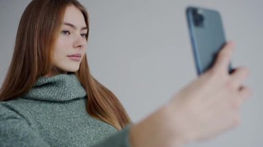 Balıkçı yaka kazaklı genç bir kadın akıllı telefonuyla özçekimini yakalıyor, yumuşak odaklanma ve doğal ışık gösteriyor. Yeşil Süveterli Genç Kadın Akıllı Telefonla Selfie Çekiyor