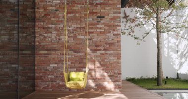 Modern bir ev bahçesi şık bir rattan salıncak, tuğla duvar ve sakin bir havuz kenarında. Rahatlama ve modern açık hava yaşam alanı için mükemmel. Wicker bahçe salıncak sandalyesi terasta asılı.