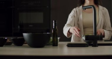 Bir kadın modern mutfak ortamında yemek hazırlıyor koyu aksanlı ve minimalist tasarımlı. İç mekan, yemek pişirme ve yaşam tarzı kavramları bu görsel olarak çekici resimde vurgulanmıştır..