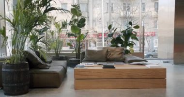 Rahat koltukları, ahşap mobilyaları ve yemyeşil bitkileri olan modern ofis lobisi. Doğal ışık odayı doldurur, sakin ve davetkar bir atmosfer yaratır..