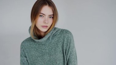 Sade bir arka planda yeşil balıkçı yaka kazak giyen sakin bir yüzü olan genç bir kadının portresi. Moda ve yaşam tarzı temaları için mükemmel.