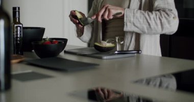 Çağdaş bir mutfakta avokado dilimleyen bir kadının yakın çekimi. Görüntü taze malzemelere ve hazırlık sürecine odaklanıyor. Modern Mutfak Ayarında Bir Avokado Hazırlayan Kadın