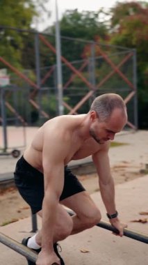 Kaslı adam parktaki paralel çubuklarda dibe vurur. Üstsüz ve antrenmanına odaklanmış durumda. Gücünü ve kendini spora adamış. Bu sağlıklı bir yaşam tarzını ve egzersizi teşvik eder.,