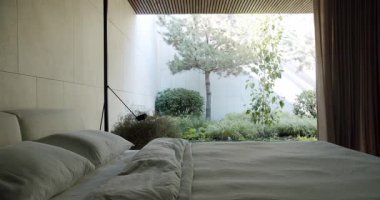 Geniş bir pencereden görülebilen yemyeşil bir bahçenin arka planına kurulmuş, yumuşak yastıklı büyük bir yatağın sergilendiği huzurlu bir yatak odası sahnesi. Geniş Pencereden Doğal Görünümü Olan Modern Yatak Odası