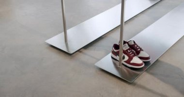 Modern bir ayakkabı mağazasında minimalist metal bir stantta sergilenen bir çift kırmızı ve beyaz spor ayakkabı. Seçimlere göz atan biri var. Chisinau, Moldova - 18 Ocak 2025