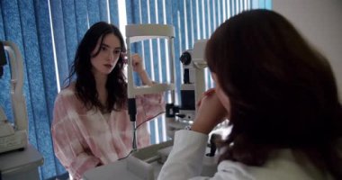 Modern aletlerle donanımlı bir klinikte kapsamlı bir göz muayenesi geçiren odaklanmış genç bir bayan hasta. Klinikte Göz Muayenesine Giden Genç Kadın