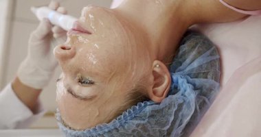 Güzellik uzmanının kaplıcaya uzanmış bir kadın müşteriye yüz maskesi uyguladığı yakın plan. Rahatlama ve cilt bakımına odaklan. Spa 'daki Kadın' a Profesyonel Yüz Bakımı. Dikey video